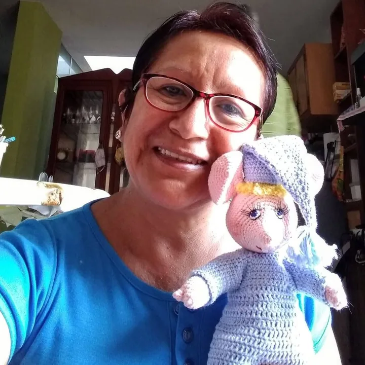 Pili sonriendo con una muñeca tejida a crochet de gorro lila